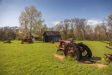 Old rusty farm equipment and tractor by a barn

