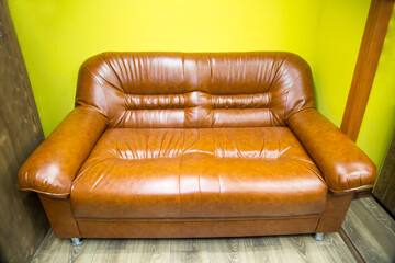 A two-seater faux leather sofa with brown armrests against a yellow wall. Interior furniture living...