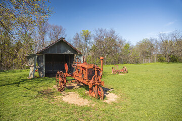 Old rusty farm equipment and tractor by a barn