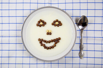 A top view of a bowl of porridge and images of the mouth, eyes, and nose laid out in white brown balls on a light-colored checkered napkin.