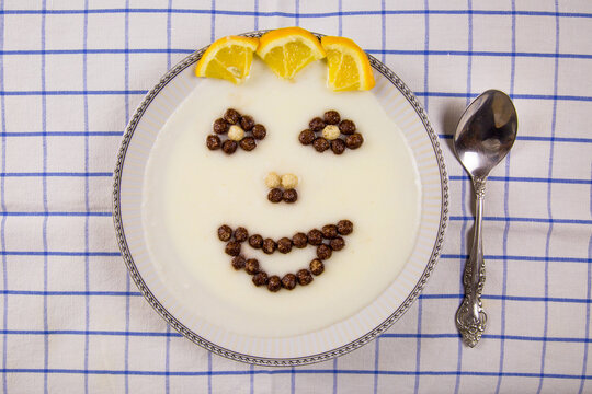 A top view of a bowl of porridge and images of the mouth, eyes, and nose laid out in white brown balls on a light-colored checkered napkin.