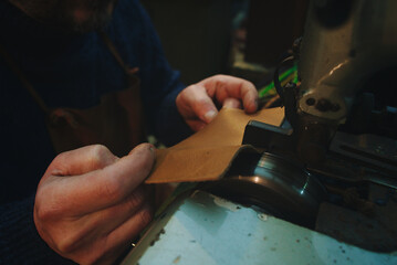 hands of craftsman work leather with thinning machinery