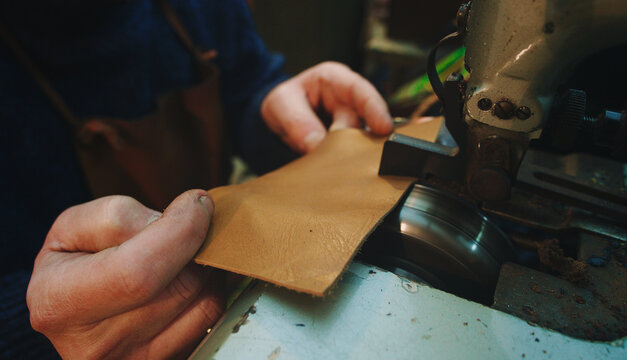 hands of craftsman work leather with thinning machinery
