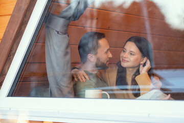 Fototapeta premium Young serene affectionate couple interacting by large window of country house
