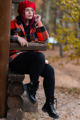 Girl sitting on a wooden bench in a checkered red coat in autumn.