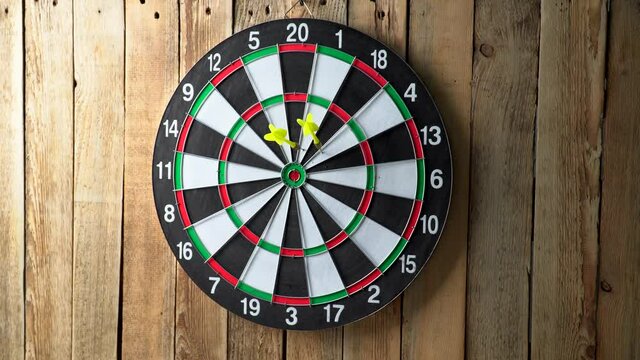 Darts game. Throwing darts at the target. A somebody throw the darts on the dart board. Dart board hanging on a wooden wall