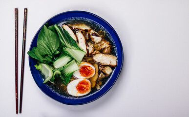 Ramen noodles with egg and bok choy in a cobalt blue bowl, chop sticks on the side