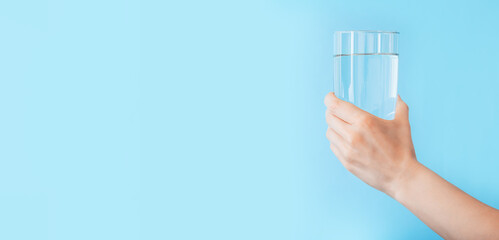 Water glass in female hand on color blue background. Long web banner with copy space. Healthy...
