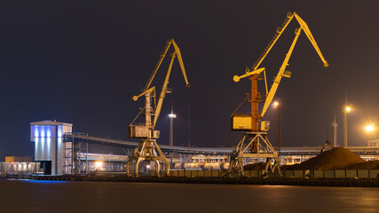 Night photo with port cranes in yellow over the Venta canal in Ventspils.