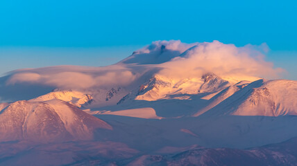 Naklejka na ściany i meble Clouds on a volcanic Erciyes mount in Kayseri. Snowy scarlet mountain. Erciyes is a large stratovolcano, reaching a height of 3,864 m it the highest mountain and most voluminous volcano of Central Ana