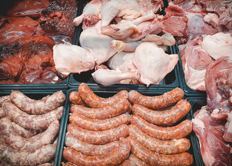 Assorted various fresh raw meat and meat products on market counter. Sausages, chicken parts and...