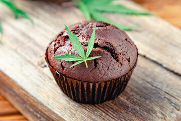 Chocolate cupcake muffins with cannabis weed cbd. Medical marijuana hemp drugs in food dessert. Cooking baking chocolate weed muffins. Cupcake with marijuana on wooden table.