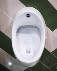 A white urinal on a green-and-white tiled wall