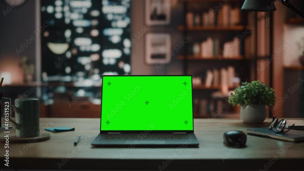 Poster Laptop Computer with Mock Up Green Screen Display Standing on the Table in Cozy Living Room. In the Background Stylish Modern Home Office Studio in the Evening with Big Cityscape Window.