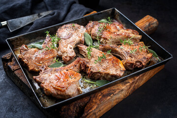Traditional barbecue dry aged veal chops served as close-up in a rustic tray on a black board