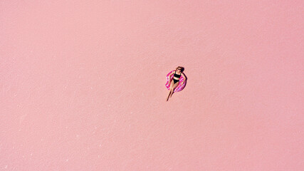 Aerial view of Beautiful woman lying in a bikini on inflatable mattress on pink salt lake. copy space. opening of the tourist season. summer holiday concept. taken from above from a drone
