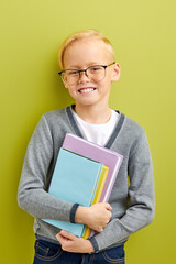 clever schoolboy with books preparing to study, smart intelligent kid in eyeglasses smiling at camera, isolated over green studio background. portrait