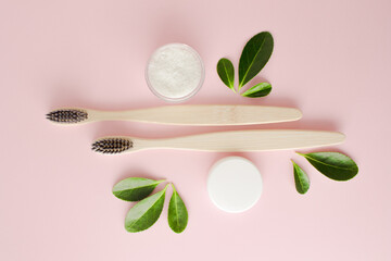 Eco-friendly bamboo toothbrushes, dentifrice and green leaf on pink background.