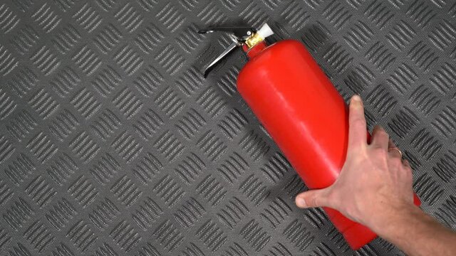 Closeup top view flatlay 4k stock video footage of male hand taking red fire extinguisher laying on black plastic rubber mat in boot of automobile