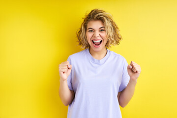 woman celebrating a victory being a winner isolated on yellow background. victory, delight concept. human facial emotions concept. trendy colors