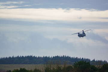 Fototapeta na wymiar RAF Chinook UH-1 helicopter flying low in a cloudy blue grey and white winter sky