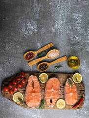 three raw steak fish trout, salmon and spices on wooden board, dark background