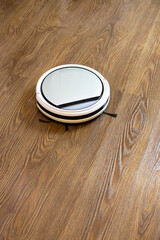 White round wireless robot vacuum cleaner on brown laminate floor. Concept everyday cleaning at home, device for help, easy household, doing chores, hygiene. Soft selective focus. Vertical