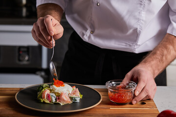 Cropped cook adding red caviar in order to spice up the dish. Male professional prepare fresh food at kitchen restaurant.