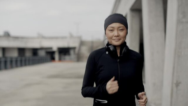 Gorgeous, asian woman jogging in urban environment, looking around and smiling. Urban city lifestyle. Active woman runner exercising outside. Sports and urban concept.