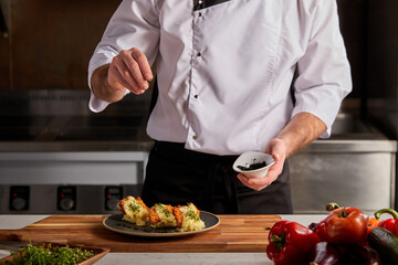 Italian cook adding spices to dish on plate, young professional chef in uniform decorating...