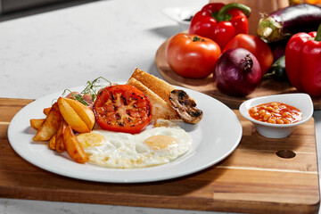 Plate with fried eggs, fries, fried bacon, crispbread, sausages, tomato in restaurant. Beautifully decorated and served dish, meal cooked by professionals. fresh vegetables in the background