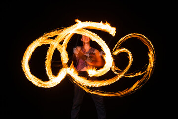 male fire dancer twirl burning baton creating sparkling trails in motion dark outdoors, twirler