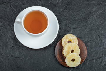 A cup of aroma tea with dried pineapple on a dark background