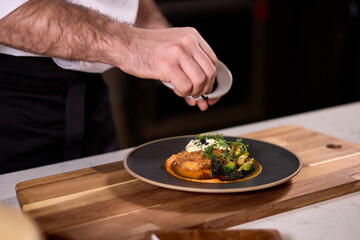 chef dressing salad with greens, adding some ingredients, chef adding finishing touch on dish before it goes on table.