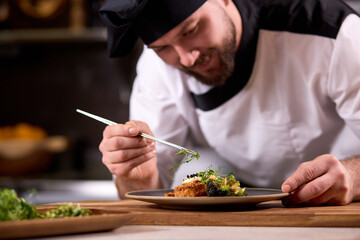 chef dressing salad with fresh greens, adding finishing touch on dish before it is going to be...