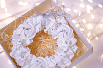 Airy white meringue in a gift box. On a white wooden background with bright lights. Very tasty dessert on family holidays.