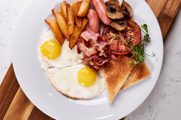 Breakfast plate with fried eggs, fries, fried bacon, crispbread, sausages, tomato in restaurant. Beautifully decorated and served dish, meal cooked by professionals