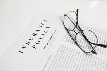 insurance policy contract with spectacles on white table. Close up view