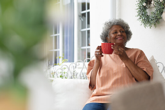 African american senior woman holding coffee cup smiling while sitting on porch of the house