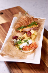 Restaurant food flat lay, croissant, cheese, grapes and vegetables on plate close-up. Dish cooked by professional for guests