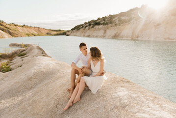 A beautiful young couple in love, a man and a woman embrace, kiss near a blue lake and sand at sunset. Vacation at the sea on the beach, sunset, morning, honeymoon, tropics, ocean, girl, relationship.