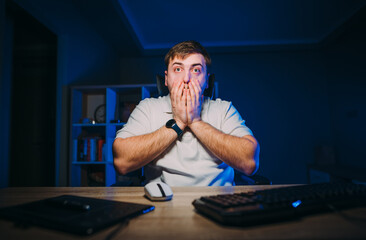 Shocked remote worker works at home on computer at night and looks at the screen with a tired face....