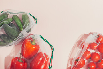 Reusable packaging of products by weight. Red bell peppers, cucumbers and tomatoes in a reusable bag on a pink background.