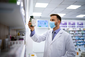 Pharmacist wearing face mask and white coat holding vitamins in pharmacy store during corona virus pandemic. Healthcare and medicine.