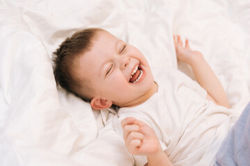 Fototapeta na wymiar A beautiful cute boy smiles and laughs while lying on a white bed