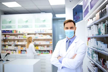  Portret van apotheker met gezichtsmasker en witte jas die in de apotheek staat tijdens de pandemie van het coronavirus. © littlewolf1989