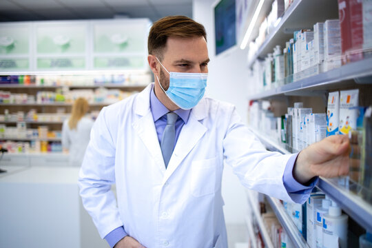 Pharmacist wearing face mask and white coat working in pharmacy store during corona virus pandemic.