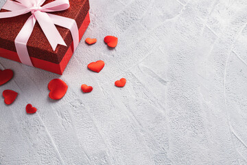 Red gift box with pink ribbon and scattered red hearts on gray background. Valentine's day or birthday concept. Place for text.