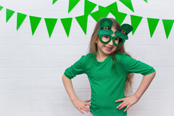 Portrait of a smiling Caucasian girl in a green T-shirt with clover leprechaun glasses on St....