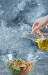 Hand pouring an oil in vegetable salad